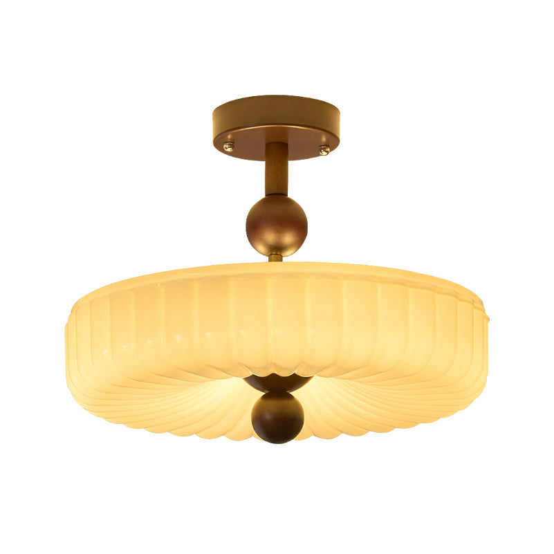 Fluted cream disc shade with radiating ribs below a walnut ball and stem, this Clérachic ceiling light lit, on white.
