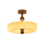 Glowing ribbed disc shade of this Clérachic ceiling light, the folds radiating to the walnut ball, on a white backdrop.