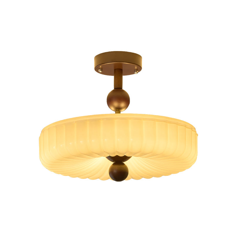 Glowing ribbed disc shade of this Clérachic ceiling light, the folds radiating to the walnut ball, on a white backdrop.