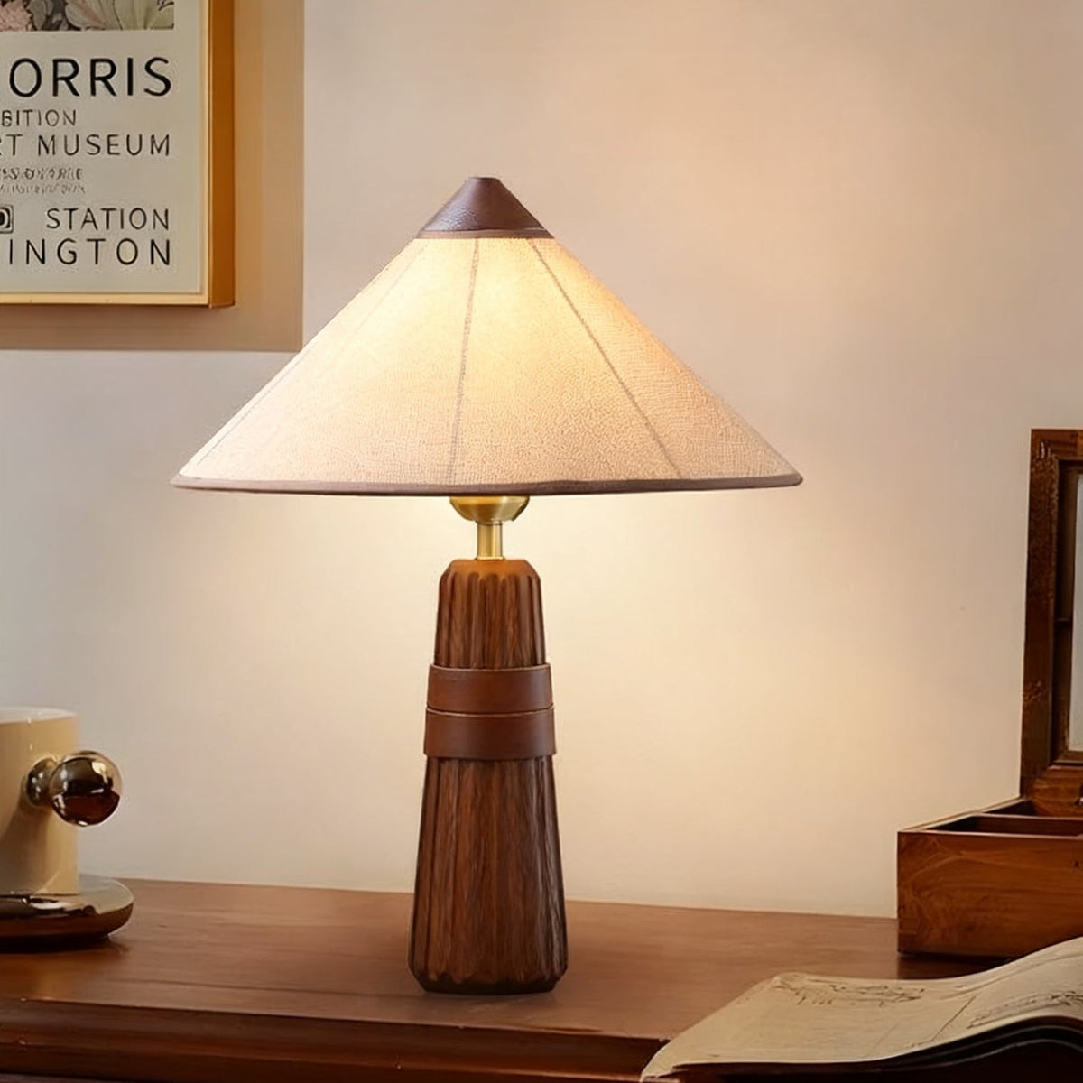 Lit Clérachic table lamp with a cone-shaped beige shade and walnut fluted base, on a wooden desk beside a framed poster.