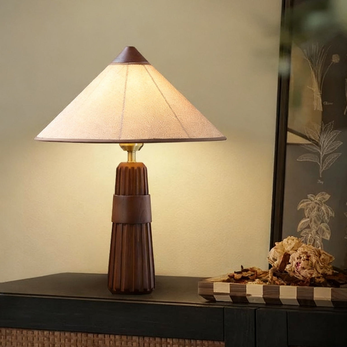 A glowing Clérachic table lamp with a walnut fluted base on a dark sideboard, next to a dried-flower arrangement on a tray.