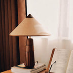 Beige-shaded Clérachic table lamp with a walnut base on stacked books, beside an open book and a sheer curtain.