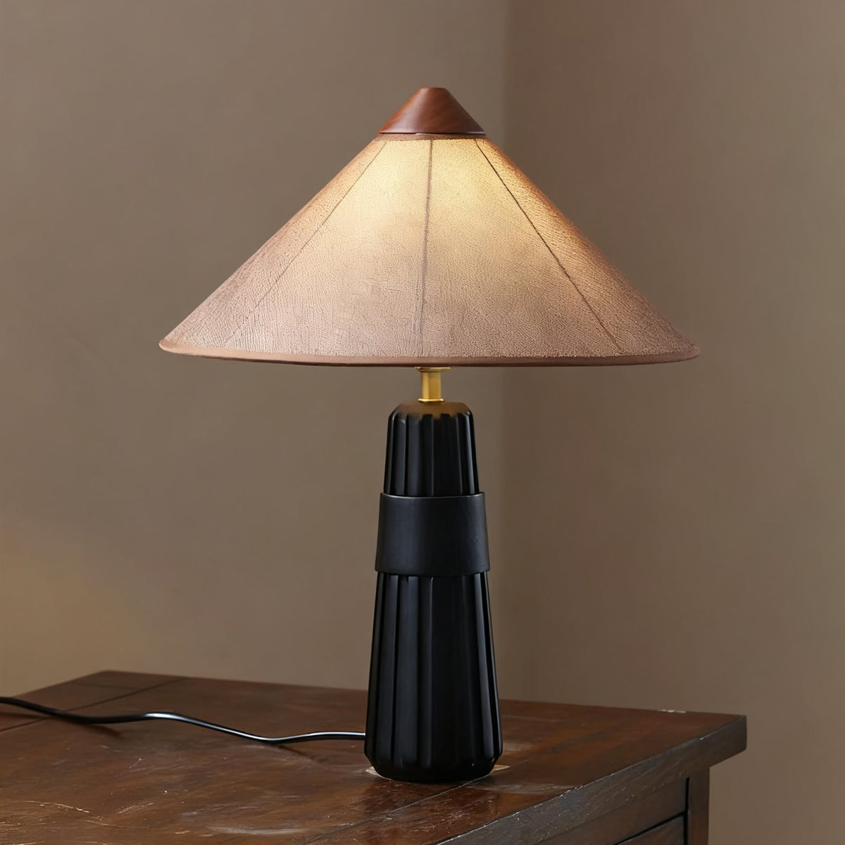 Black fluted-base Clérachic table lamp with a muted pink-beige cone shade, on a dark wooden surface beside a window.
