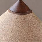 Close view of the woven beige fabric shade and the walnut cap on this Clérachic table lamp.