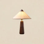 Walnut-base Clérachic table lamp with a cone shade, lit and shown against a plain warm cream backdrop.