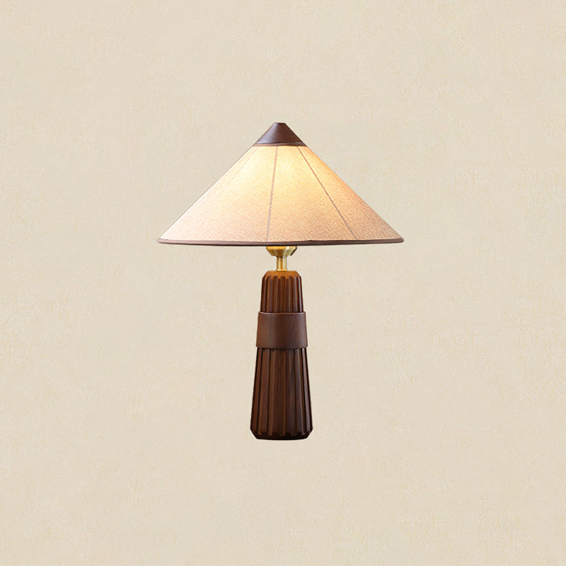 Walnut-base Clérachic table lamp with a cone shade, lit and shown against a plain warm cream backdrop.