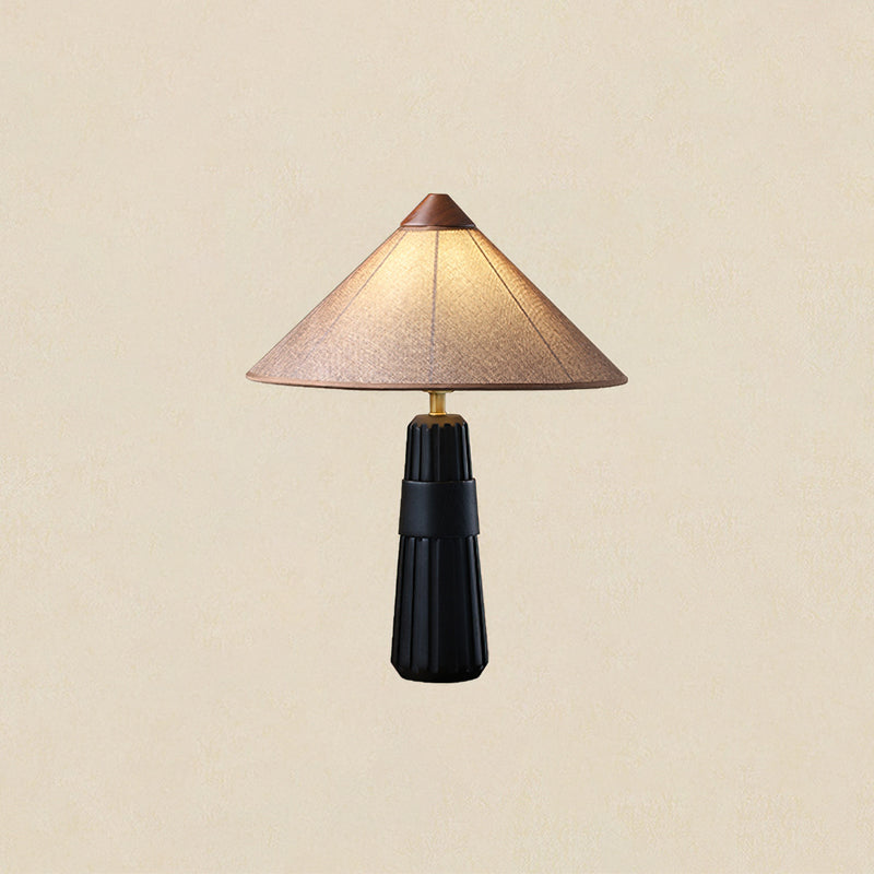 Black-base Clérachic table lamp with a pink-beige cone shade and wooden cap, lit against a plain warm cream backdrop.