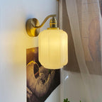 Side view of the lit Clérachic Fluted White Glass Wall Sconce, the shade creamy where the bulb sits behind eight shallow flutes.