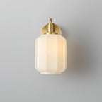 Front view of the lit Clérachic Fluted White Glass Wall Sconce, the fluted shade centred with only the brass collar showing.