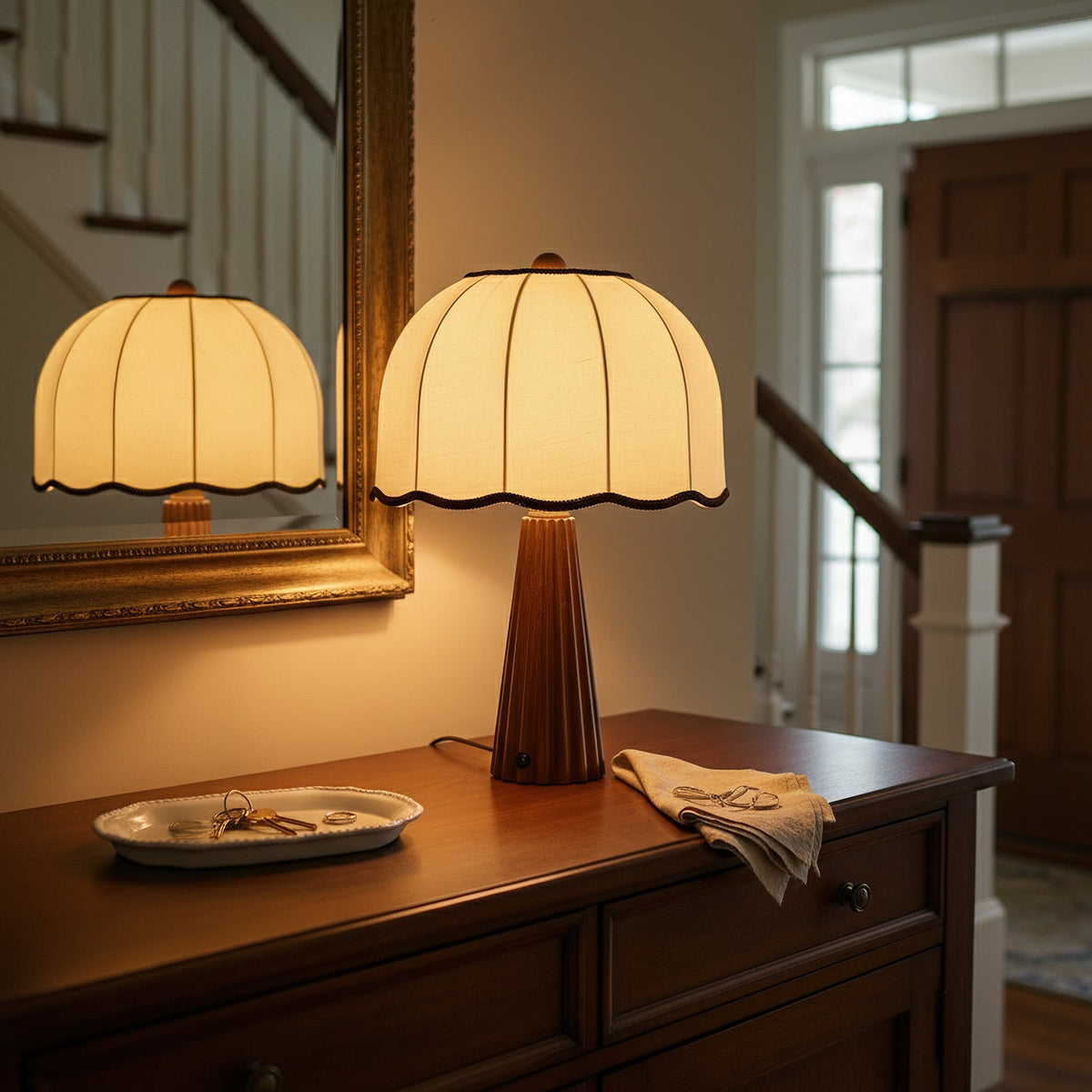 Lit Clérachic table lamp with a scalloped cream shade on a wooden console, its glow repeated in a gilt-framed mirror.