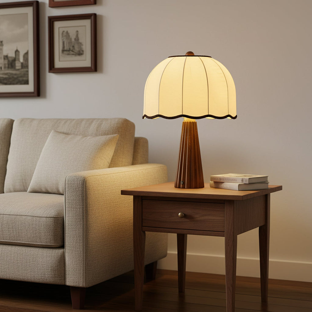 A Clérachic table lamp with a cream dome shade on a small walnut side table beside a textured armchair and a stack of books.