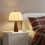 Clérachic table lamp glowing on a white bedside table next to a tartan duvet, with a cup and a book at its foot.