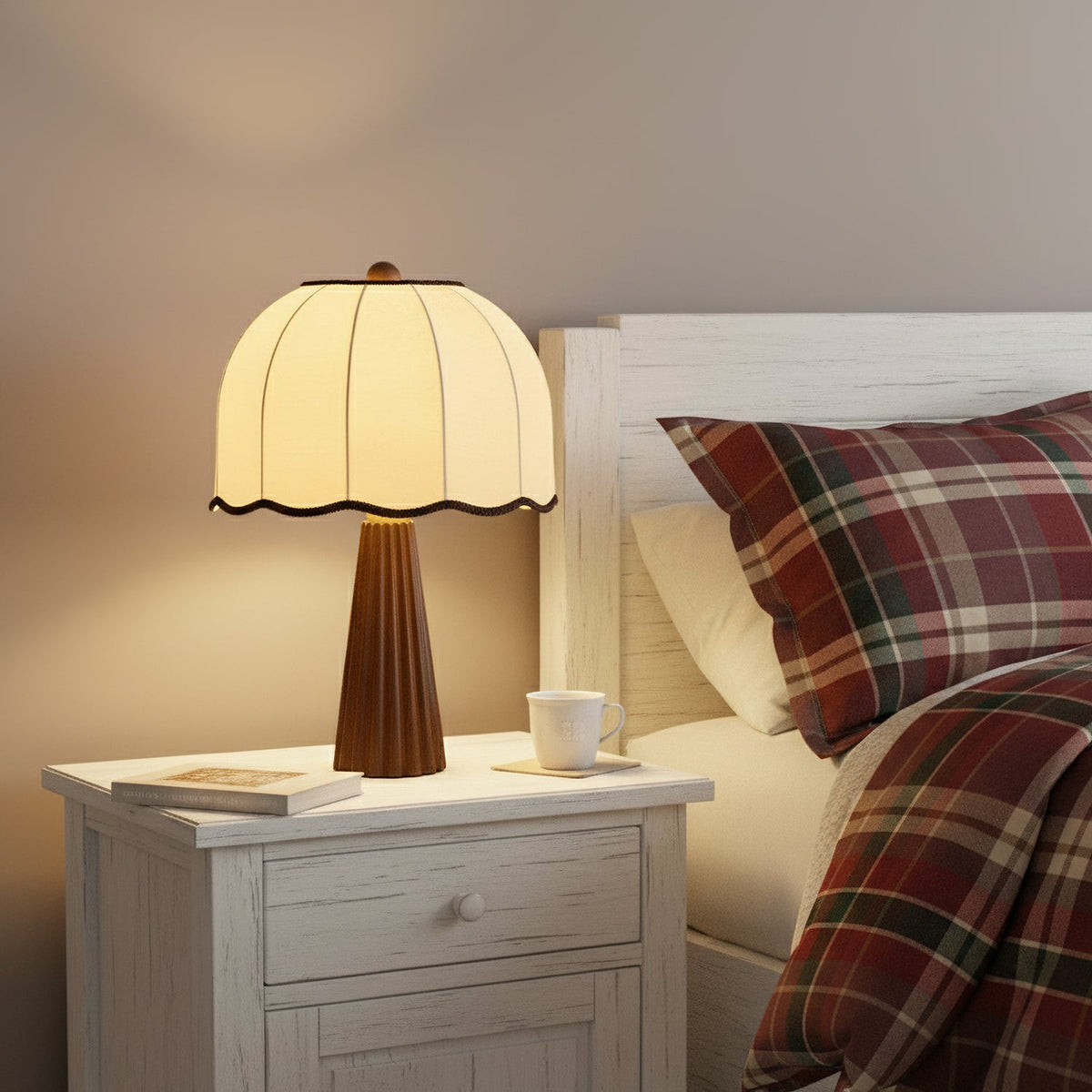 Clérachic table lamp glowing on a white bedside table next to a tartan duvet, with a cup and a book at its foot.