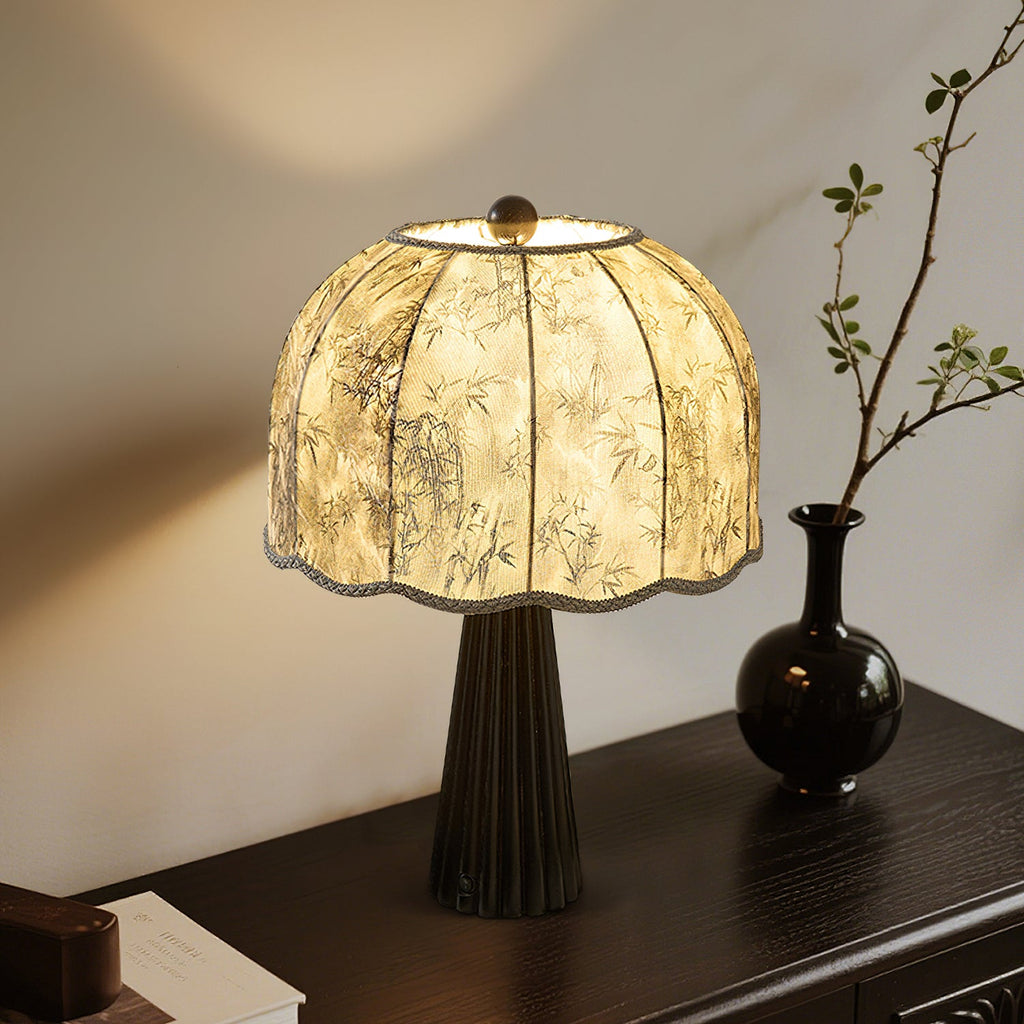 Black-based Clérachic table lamp with a grey bamboo-print shade glowing on a dark wooden console beside a black vase and a branch.