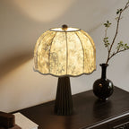 Black-based Clérachic table lamp with a grey bamboo-print shade glowing on a dark wooden console beside a black vase and a branch.
