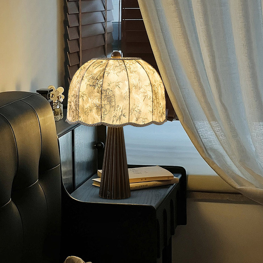 Clérachic table lamp with a patterned shade and fluted dark base on a black cabinet, shown beside a window with a pale curtain.