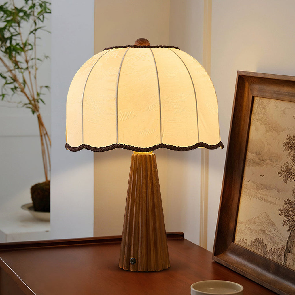 Clérachic table lamp lit on a wooden desk, its dome shade with ribbed seams and a fluted walnut-colour base, beside a framed landscape.