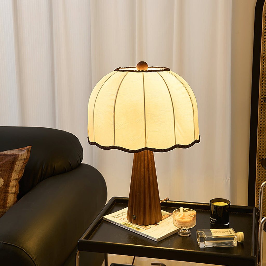A lit Clérachic table lamp on a black side tray with a candle and a book, in front of white curtains and a dark leather armchair.