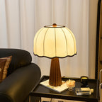 A lit Clérachic table lamp on a black side tray with a candle and a book, in front of white curtains and a dark leather armchair.