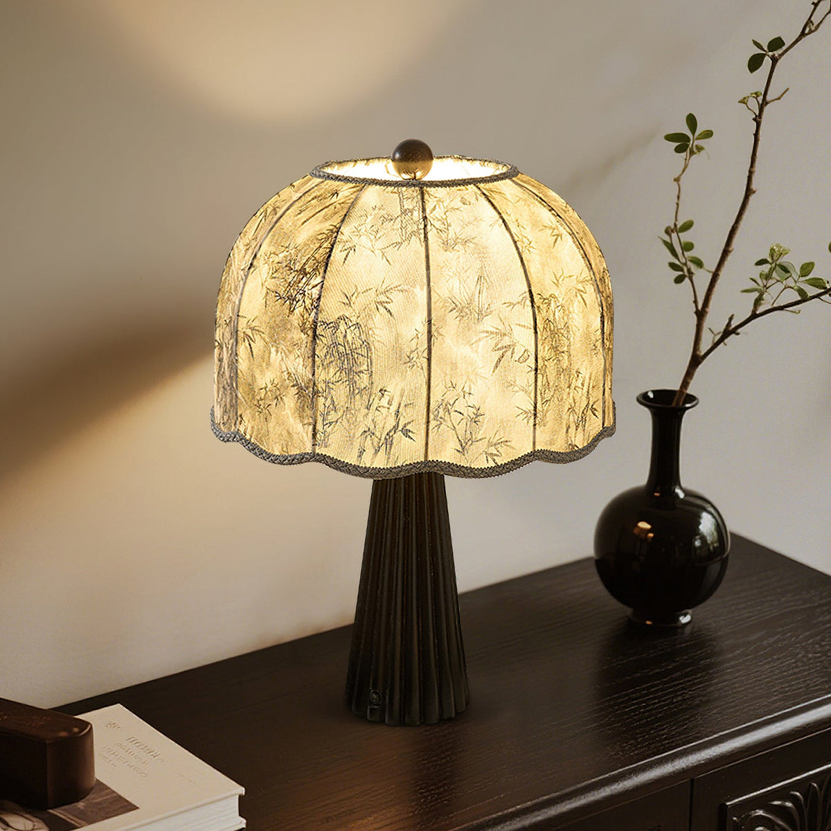 Clérachic black table lamp with a bamboo-print shade lit in a corner, with a dark vase and a leafy branch on a console.