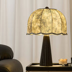 Clérachic table lamp with a black fluted base and a printed scalloped shade, glowing on a black tray beside a candle and a dark chair.