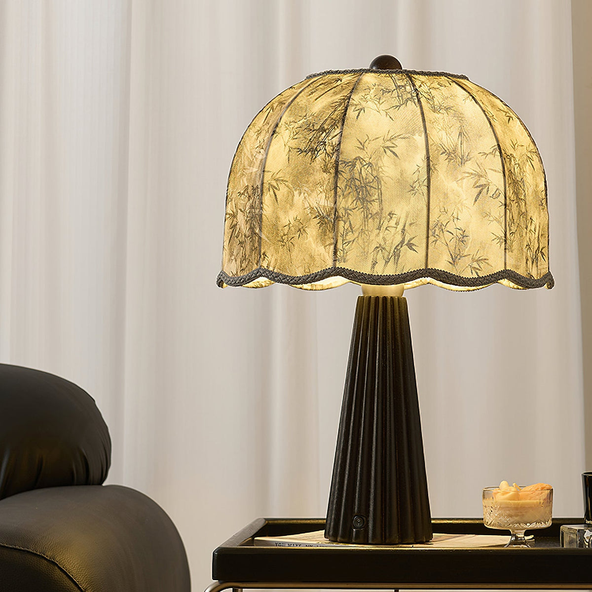 Clérachic table lamp with a black fluted base and a printed scalloped shade, glowing on a black tray beside a candle and a dark chair.