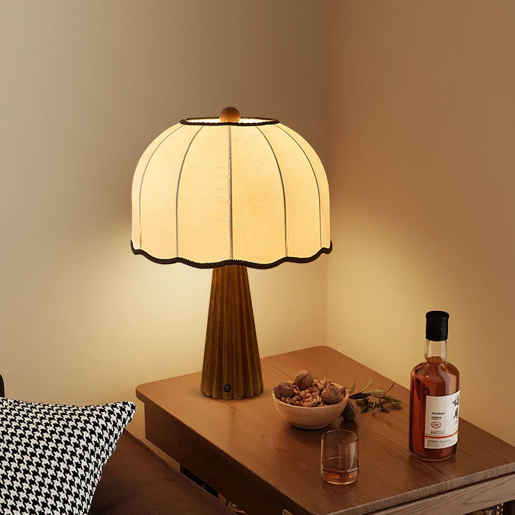 Lit Clérachic table lamp with a cream dome shade on a wooden side table with a bowl of nuts and a glass of whisky beside it.