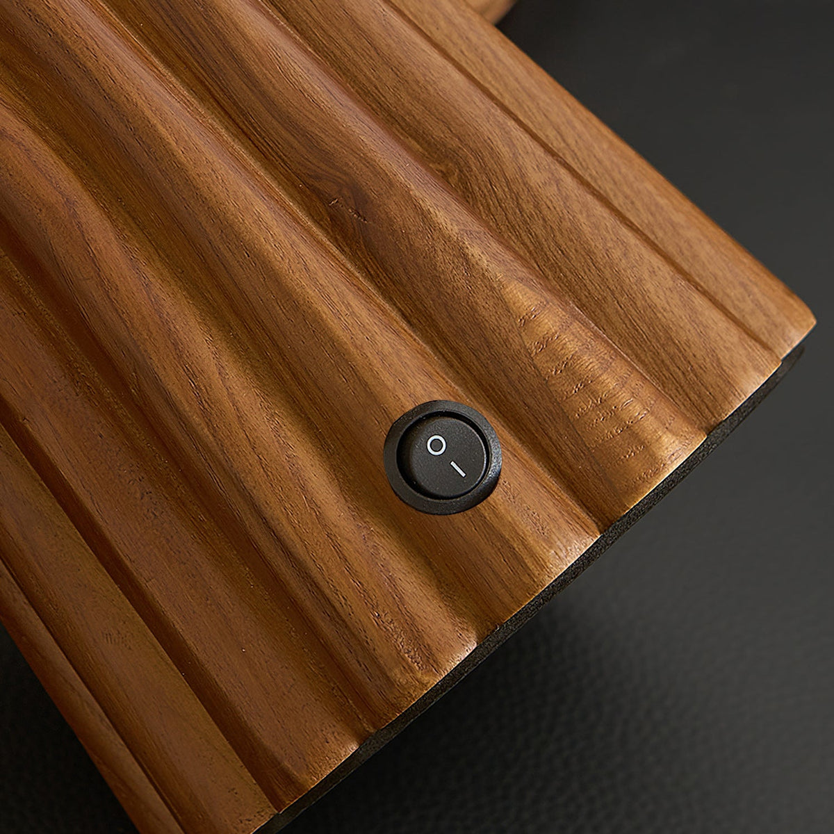 Close view of the fluted walnut-colour wood and the small round on-off switch on the base of this Clérachic table lamp.