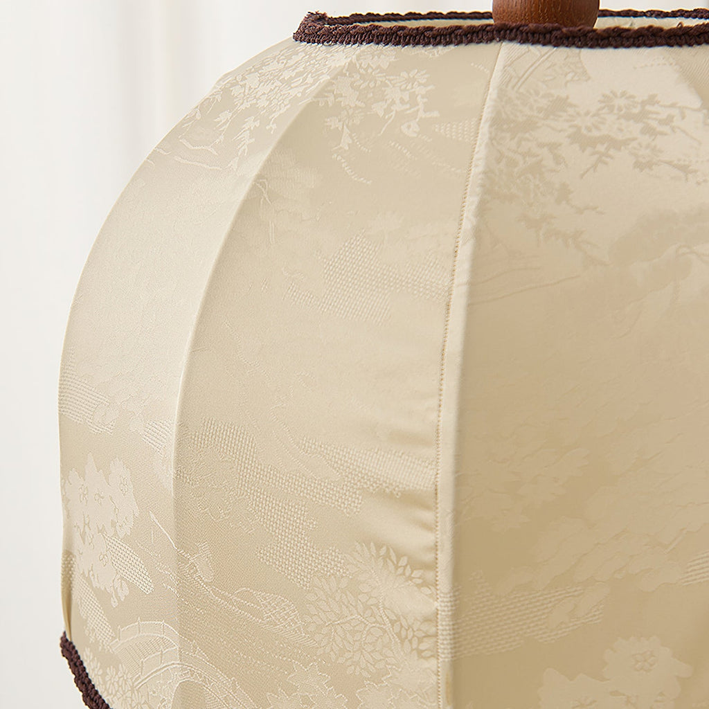 Close view of the woven cream fabric with a faint floral pattern and dark braid trim on this Clérachic lamp shade.