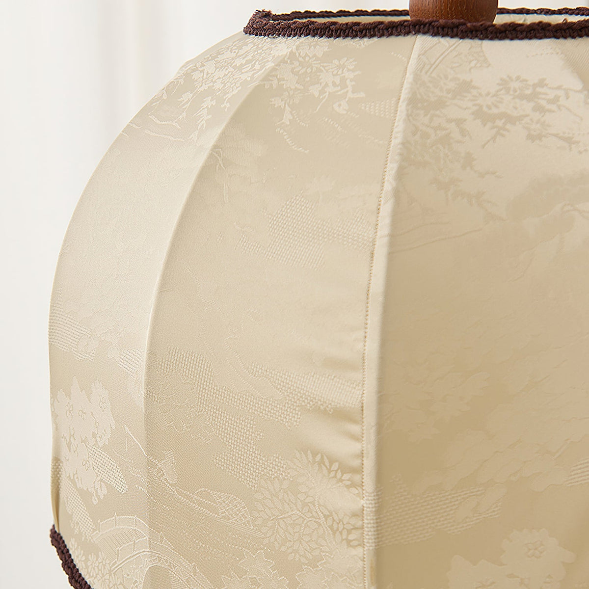 Close view of the woven cream fabric with a faint floral pattern and dark braid trim on this Clérachic lamp shade.