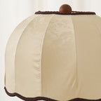 Close view of the cream dome shade with its ribbed panel seams, wooden knob on top and dark scalloped braid on this Clérachic lamp.
