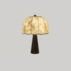 Black-based Clérachic table lamp lit, its bamboo-print dome shade glowing on a light grey background.
