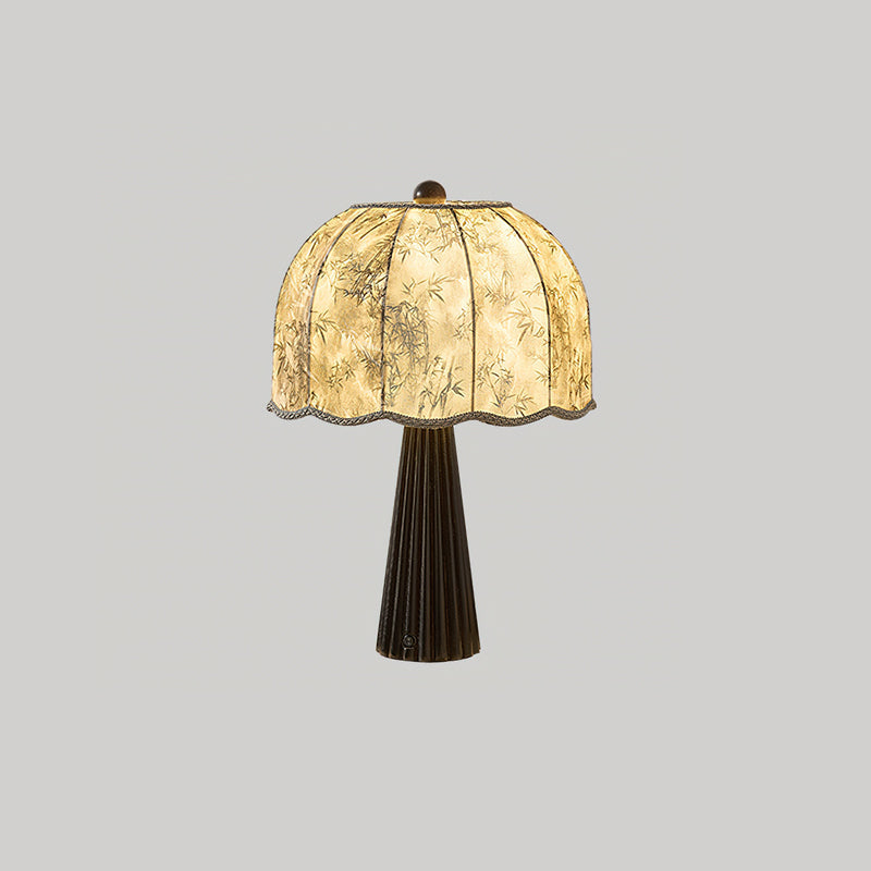 Black-based Clérachic table lamp lit, its bamboo-print dome shade glowing on a light grey background.