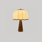 Walnut-colour Clérachic table lamp lit on a grey backdrop, with a cream dome shade and fluted wooden base.