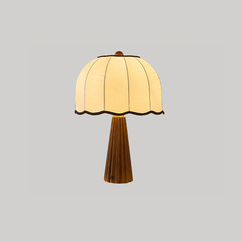 Walnut-colour Clérachic table lamp lit on a grey backdrop, with a cream dome shade and fluted wooden base.