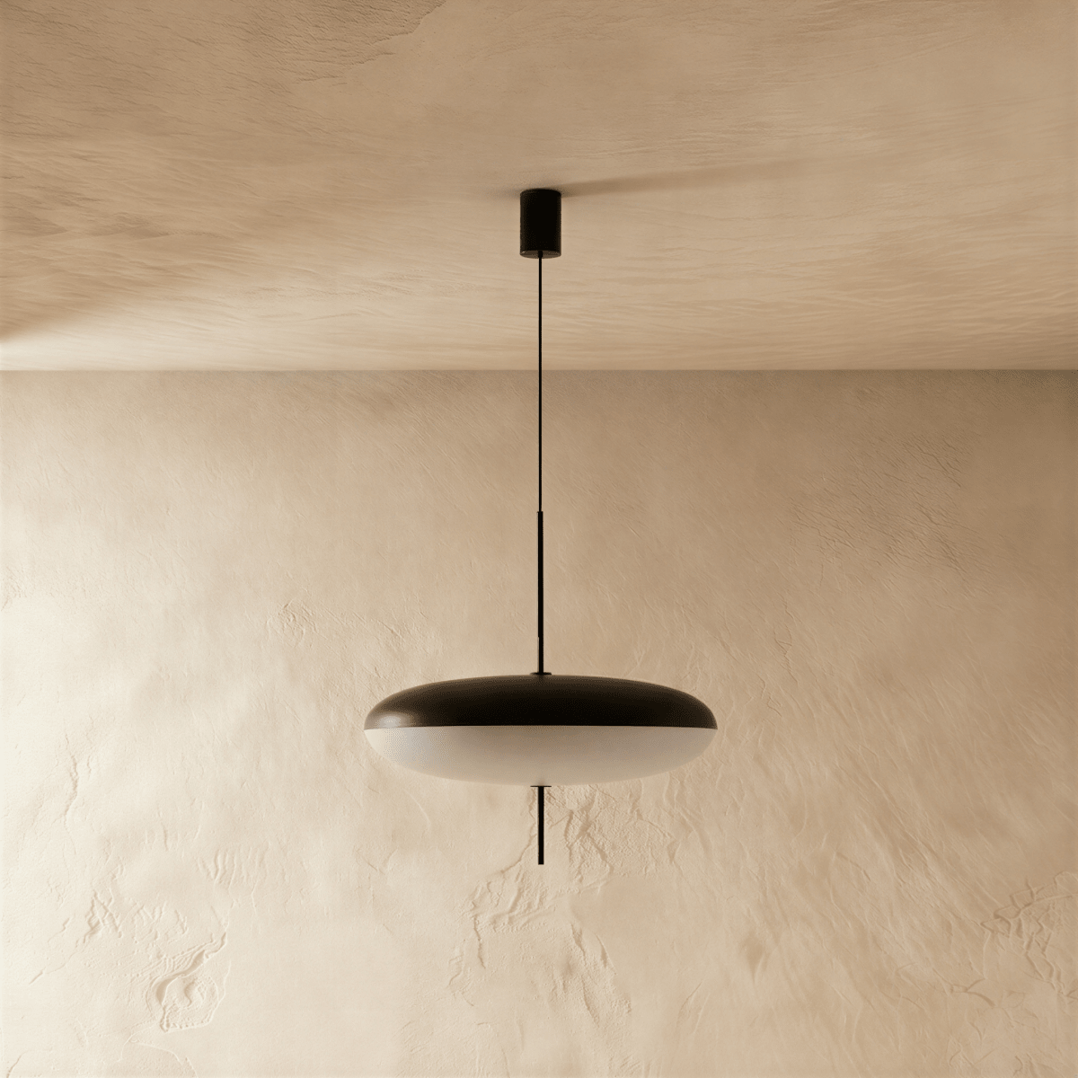 Clérachic saucer pendant in black and white, hung on a slim black stem from a round black canopy against a pale plaster wall.
