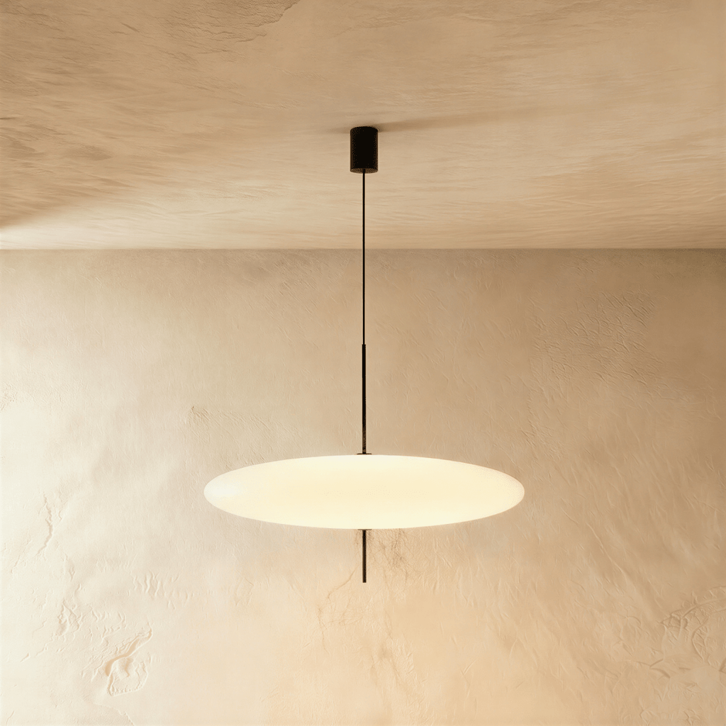 Clérachic wide all-white saucer pendant with a smooth opal diffuser on a slim black rod, lit against a textured plaster wall.