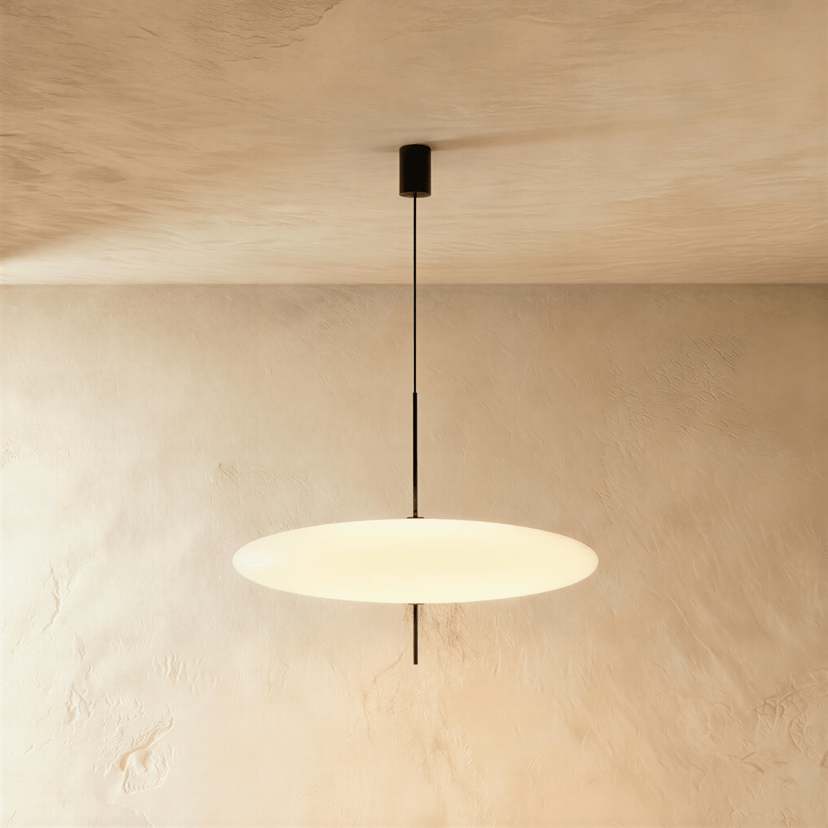 Clérachic wide all-white saucer pendant with a smooth opal diffuser on a slim black rod, lit against a textured plaster wall.