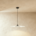 Clérachic flat frosted disc pendant with a black cone cap and dark centre panel, on a black cord against limewash plaster.