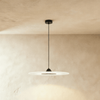 Clérachic flat frosted disc pendant with a black cone cap and dark centre panel, on a black cord against limewash plaster.