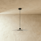 Clérachic slim frosted acrylic disc pendant in black fittings, hung from a round ceiling rose beside a plaster wall.