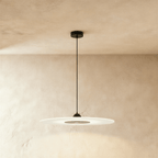 Clérachic large frosted disc pendant with black fittings, glowing softly beneath a limewash plaster ceiling and wall.