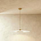 Clérachic broad frosted disc pendant in gold, its brass-toned centre panel glowing under a plaster ceiling.