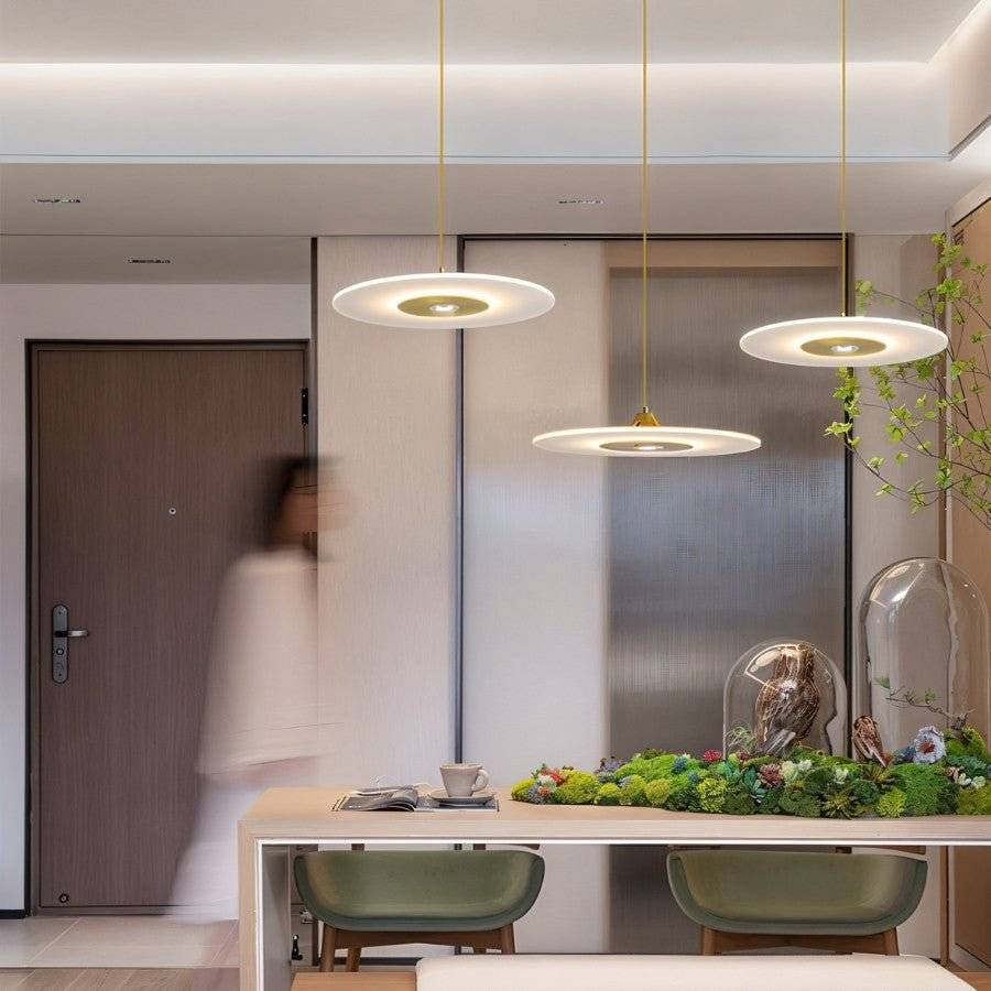 Clérachic three gold-centred disc pendants at different heights above a pale wooden table with green stools.