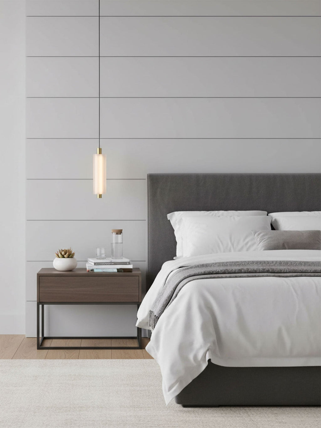 A small single-head Clérachic pendant hangs in front of a panelled wall, beside a grey bed and a dark metal bedside table.
