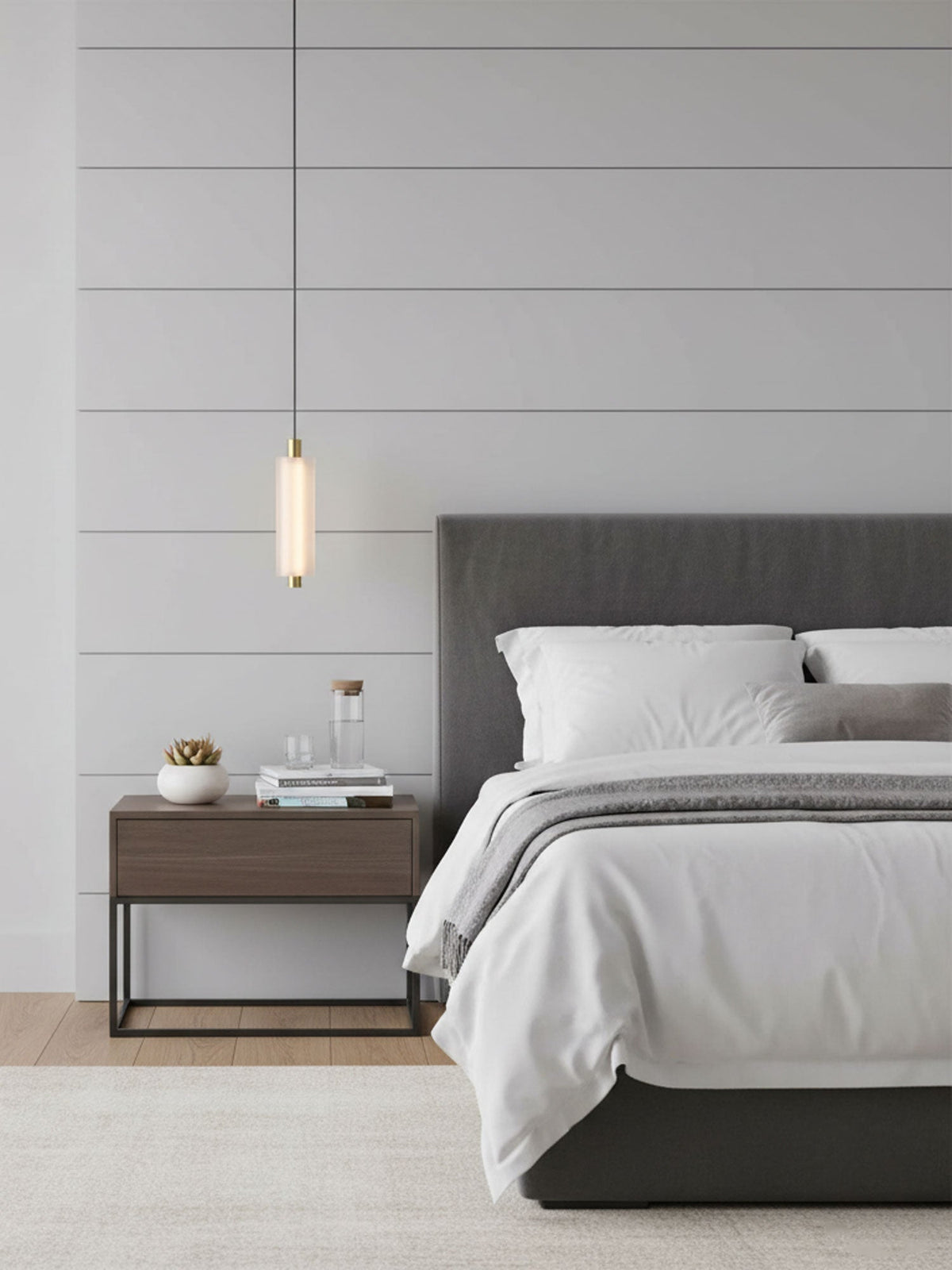 A small single-head Clérachic pendant hangs in front of a panelled wall, beside a grey bed and a dark metal bedside table.