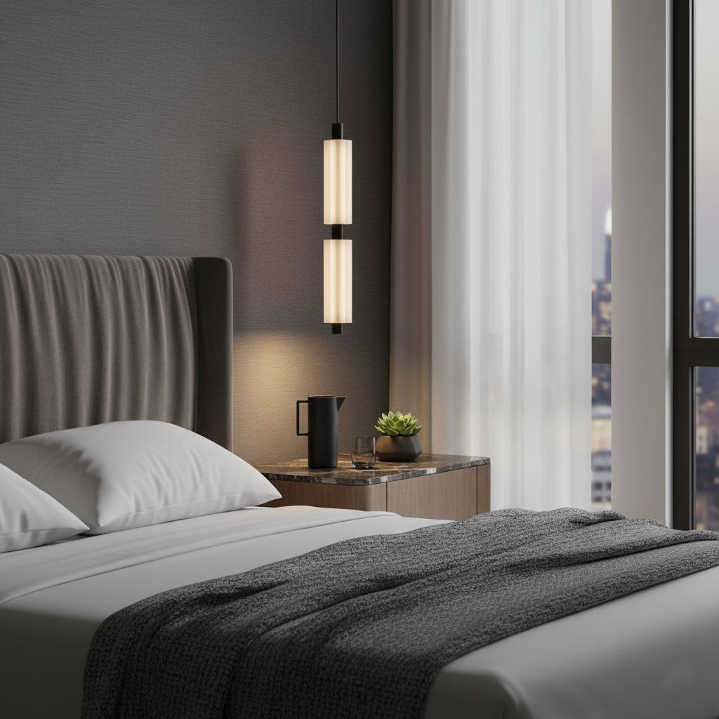 The soft glow of a two-head Clérachic pendant sits above a bedside shelf, with a charcoal throw on the bed below.