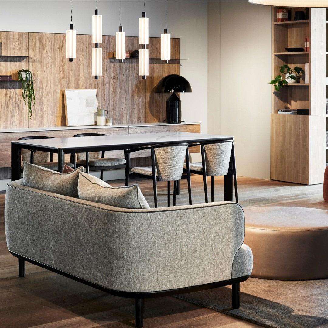 A group of Clérachic pendants hangs above a dining table, behind a grey sofa and a timber-clad wall with shelves.