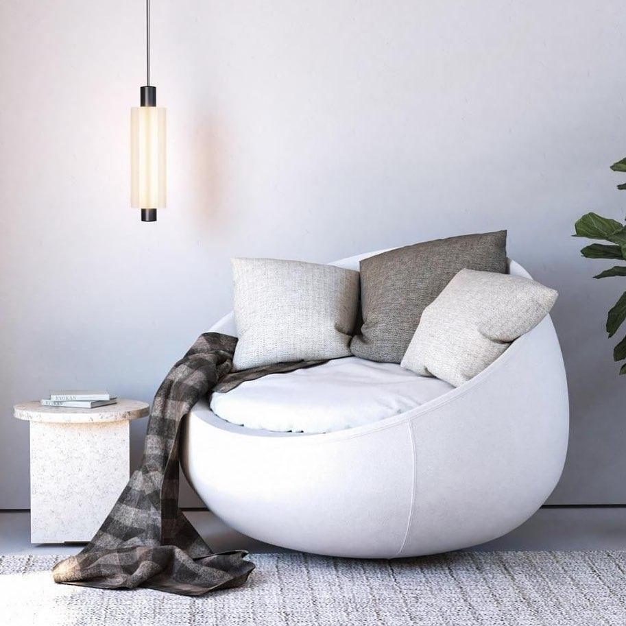 A single-head Clérachic pendant with a black cap hangs above a white round armchair with a checked throw.