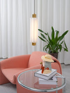 A frosted Clérachic pendant with gold ends hangs above a coral armchair, with a glass side table and a leafy plant.